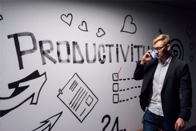 Image d'un jeune homme blond avec un portable a l'oreille qui passe devant un mur ou le mot PRODUCTIVITY est inscrit